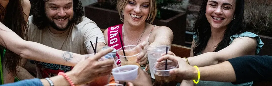 People toasting their plastic drink cups and smiling.
